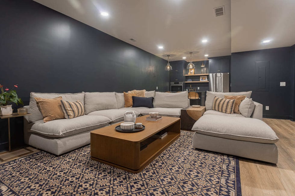 Cozy basement living room with sectional sofa, patterned rug, and bar area in the background in a Cincinnati home