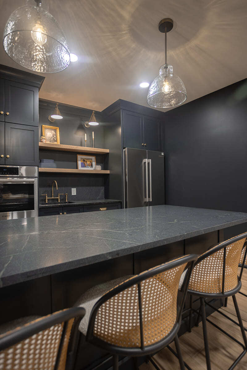 Modern basement bar with dark cabinetry, stone island, pendant lights, and woven bar stools in a Cincinnati home