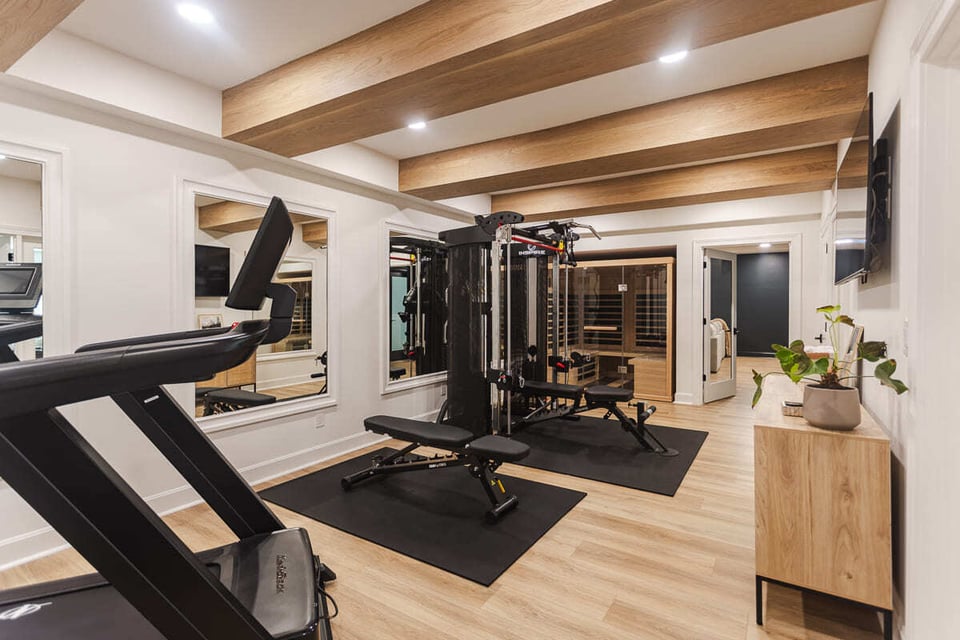 Modern home gym with treadmill, weight machine, mirrors, and exposed wood beams, located in Cincinnati