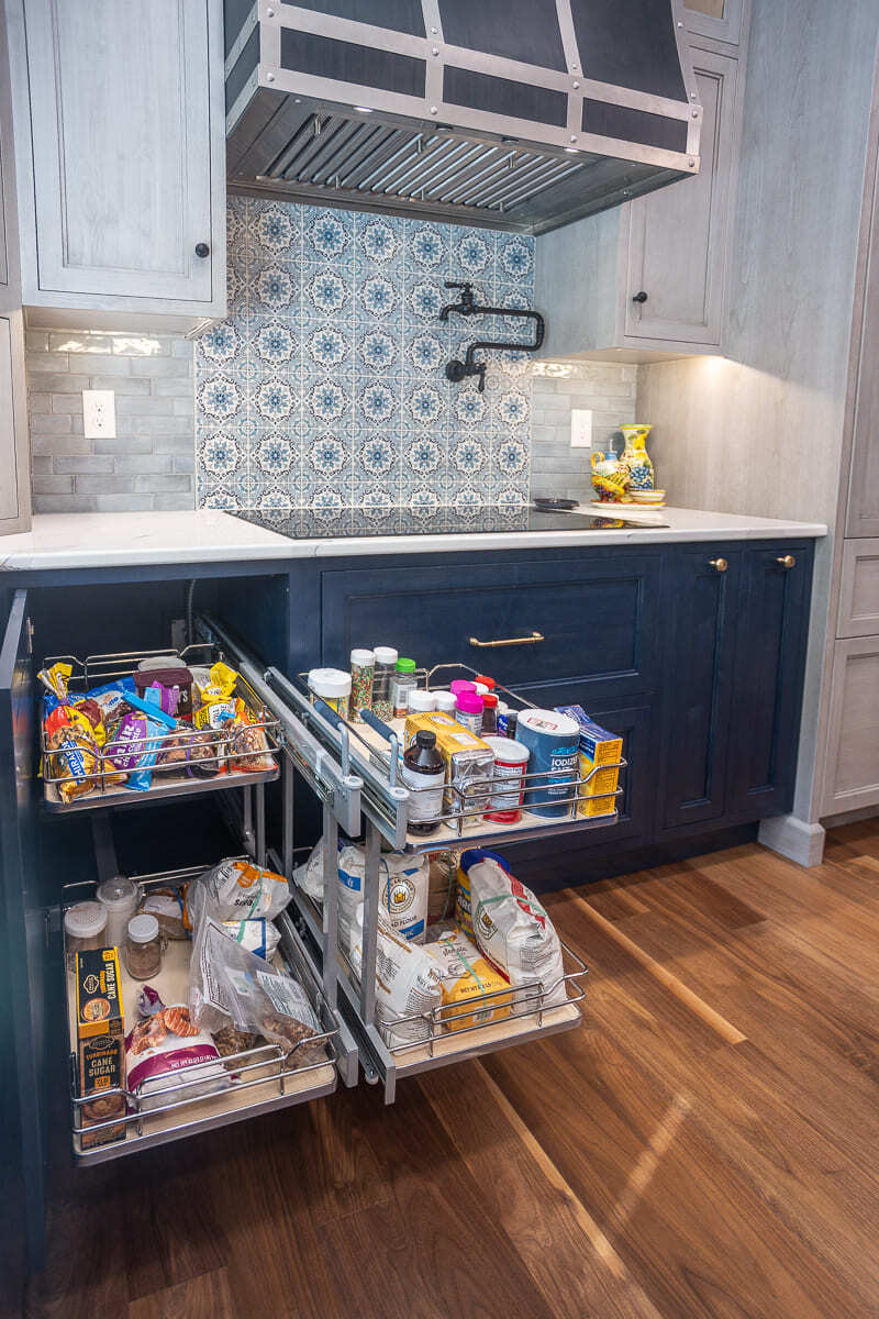 Amish-built kitchen cabinets with pull-out pantry storage, patterned tile backsplash, and custom range hood.