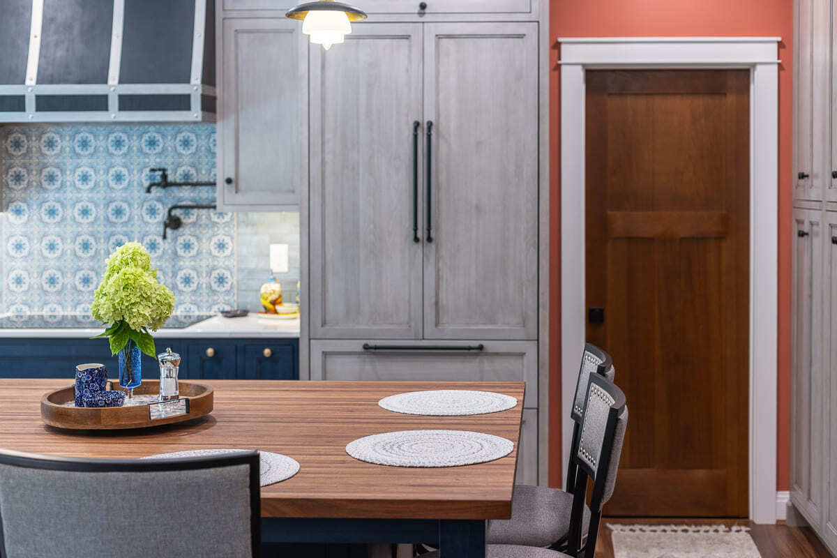 Custom kitchen island with wood top, gray Amish-built cabinets, blue tile backsplash, and pantry-style storage.