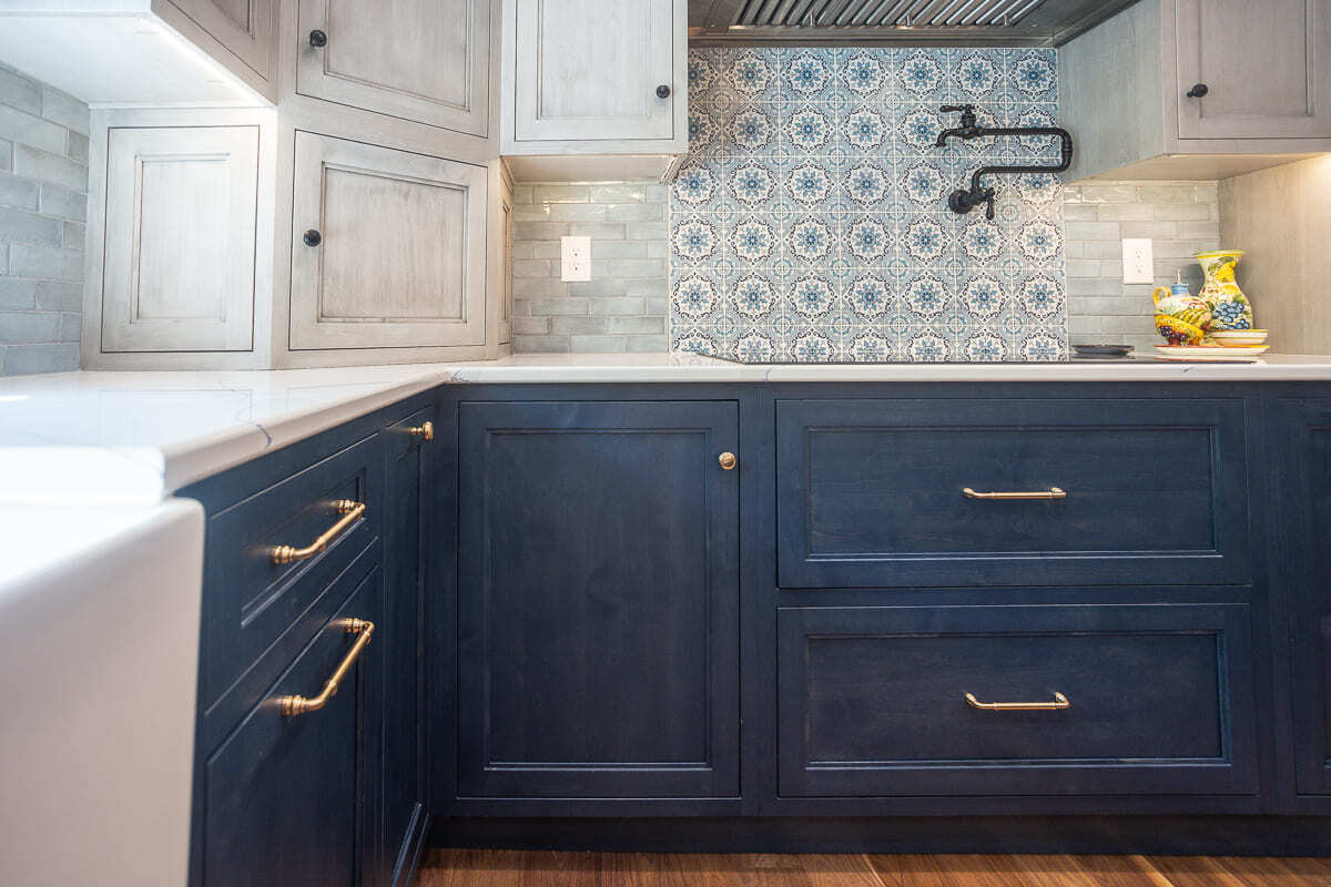 Two-tone Amish-built kitchen cabinets with brass hardware, quartz counters, and patterned tile backsplash.