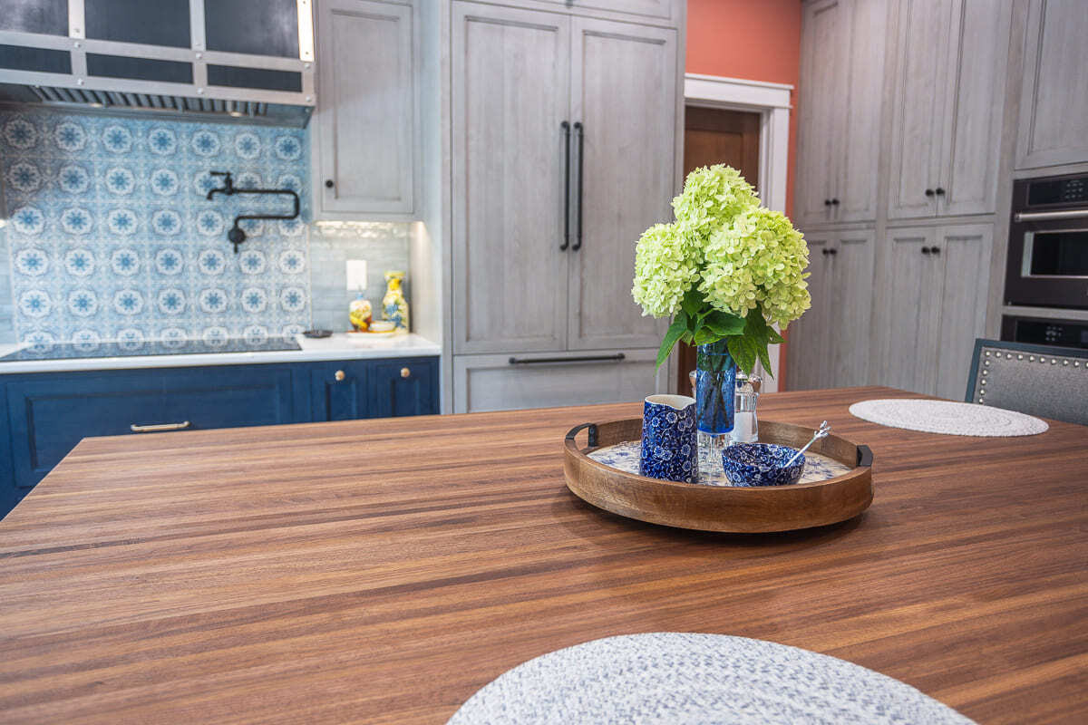 Wood island countertop with blue and gray Amish-built cabinets, patterned backsplash, and custom range hood.