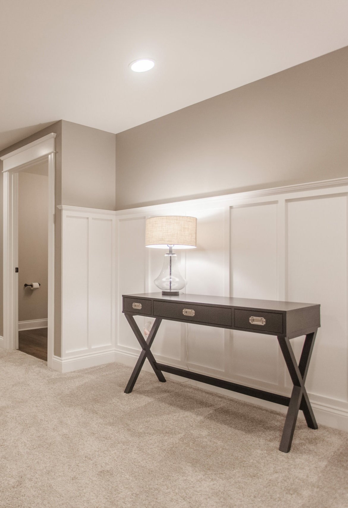Amberly Village, OH basement hallway with white wainscoting, carpet, console table, and lamp