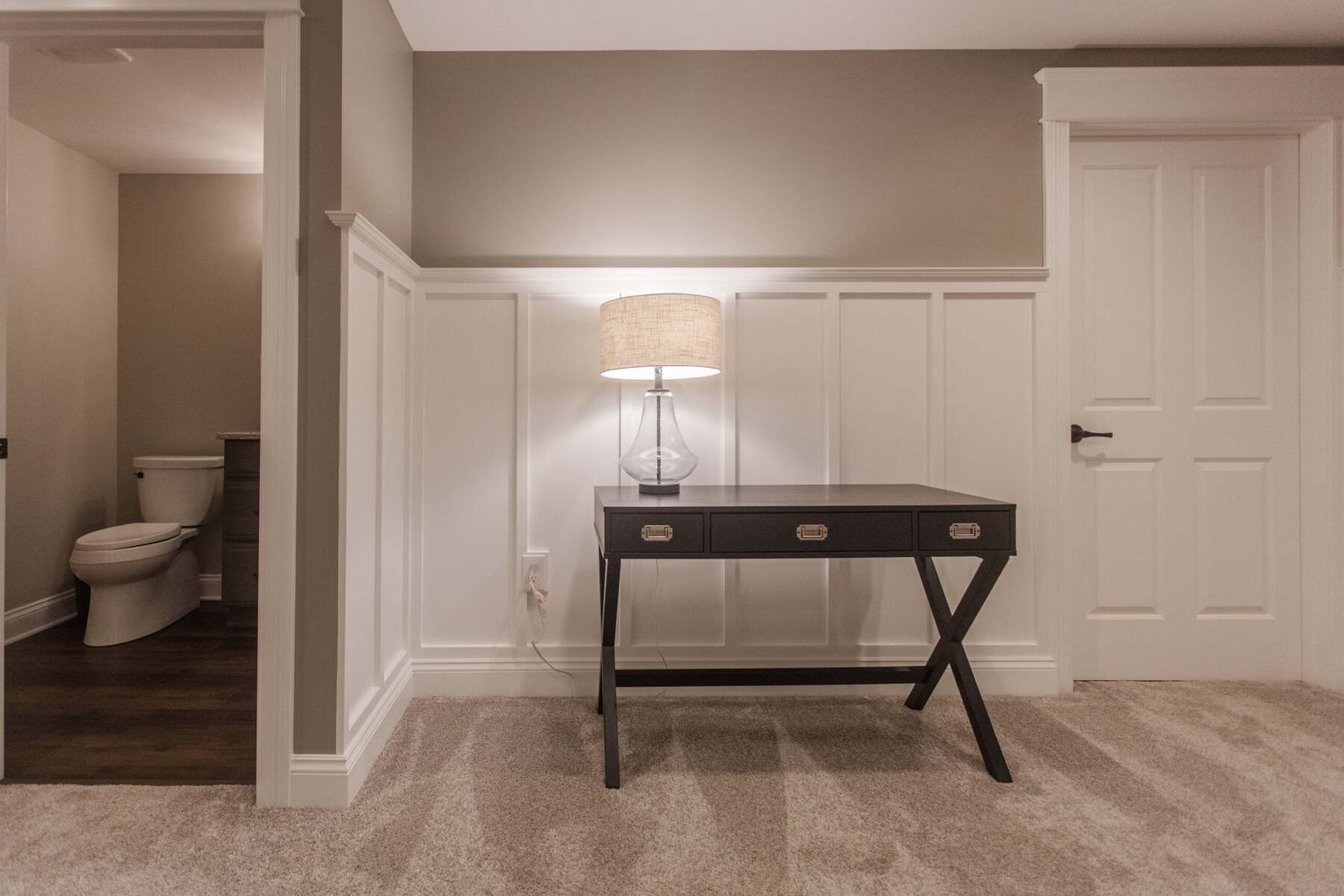 Amberly Village, OH basement hallway with white wainscoting, console table, lamp, and nearby bathroom