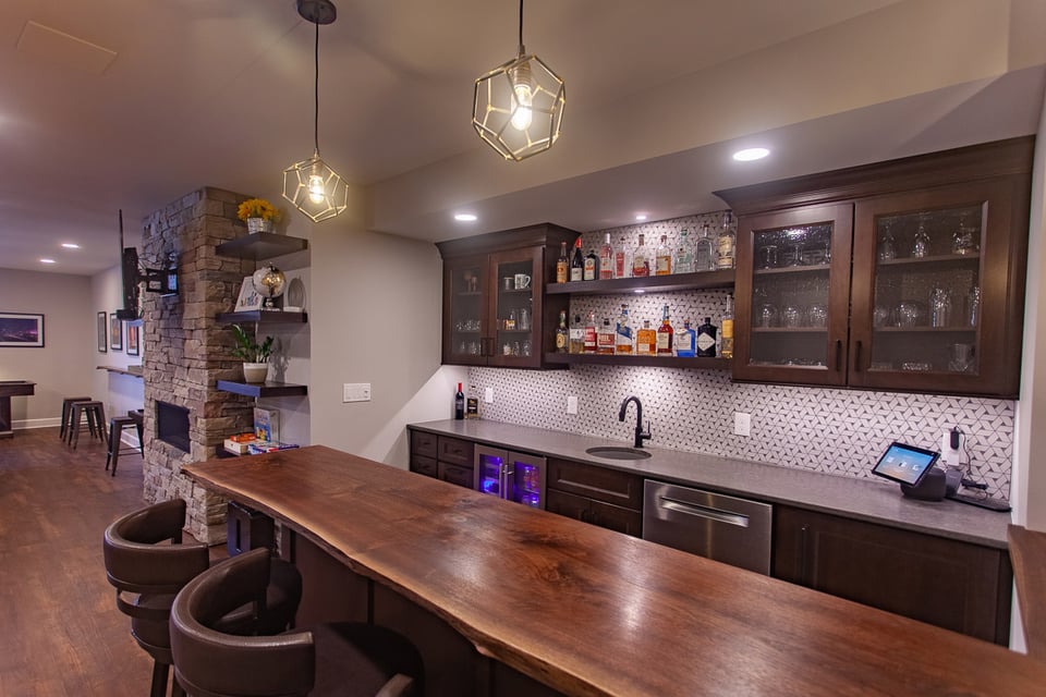 Basement bar remodel by Legacy Builders featuring a wood countertop, glass cabinets, and a modern backsplash