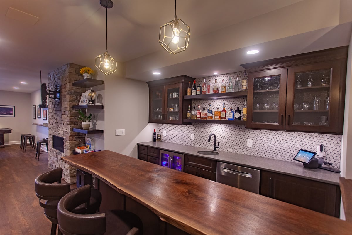 Basement bar remodel by Legacy Builders featuring a wood countertop, glass cabinets, and a modern backsplash