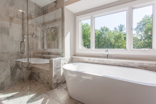 Bright Cincinnati bathroom with freestanding tub, walk-in shower, and large window with wooded view