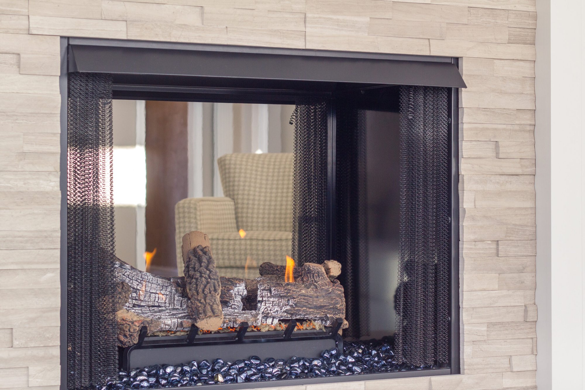 Cincinnati fireplace with glass front, burning logs, stone surround, and modern black frame detail in a cozy living space