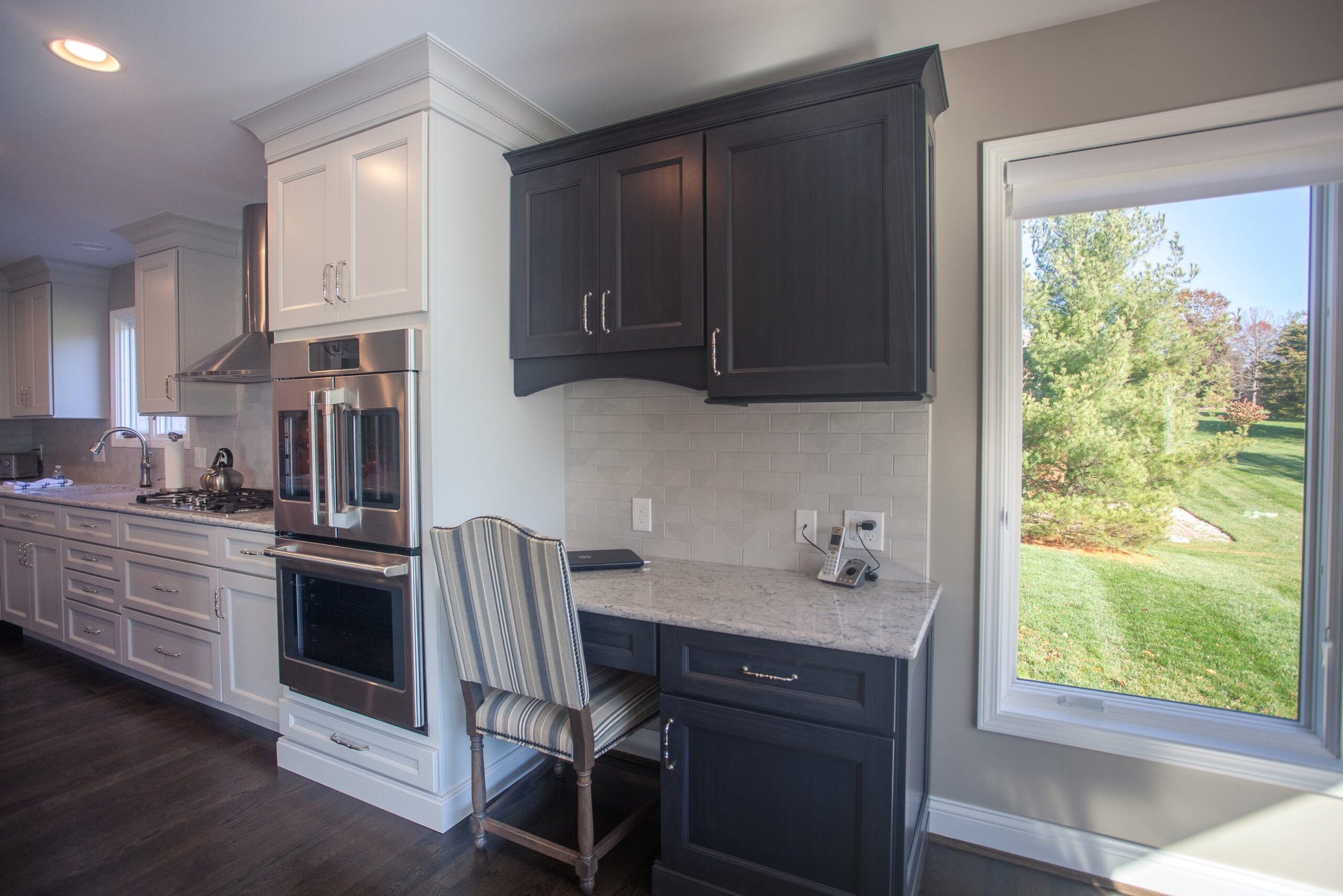 Cincinnati kitchen with built-in desk nook, white and dark cabinetry, window view, and stainless appliances in a bright open space