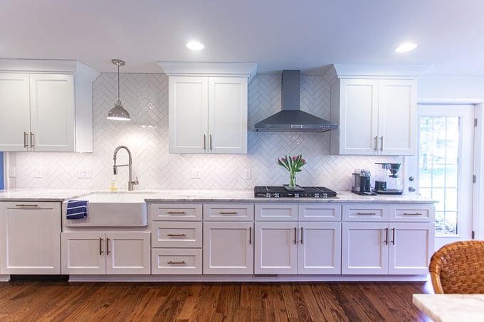 Cincinnati kitchen with white cabinets, farmhouse sink, herringbone tile backsplash, stainless steel appliances, and hardwood floors