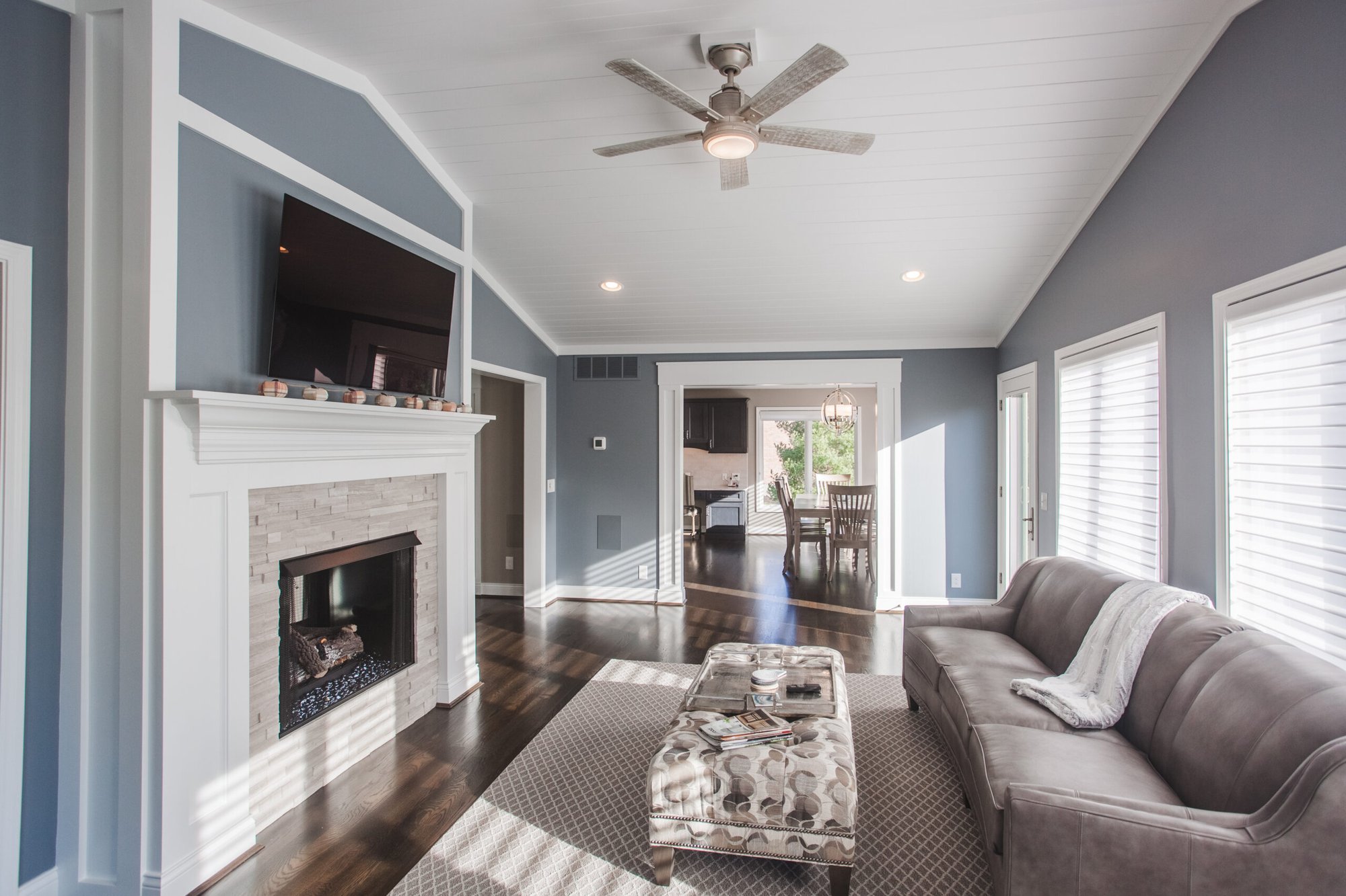Cincinnati living room with fireplace, wall-mounted TV, gray sofa, ceiling fan, and hardwood floors in a bright, open layout