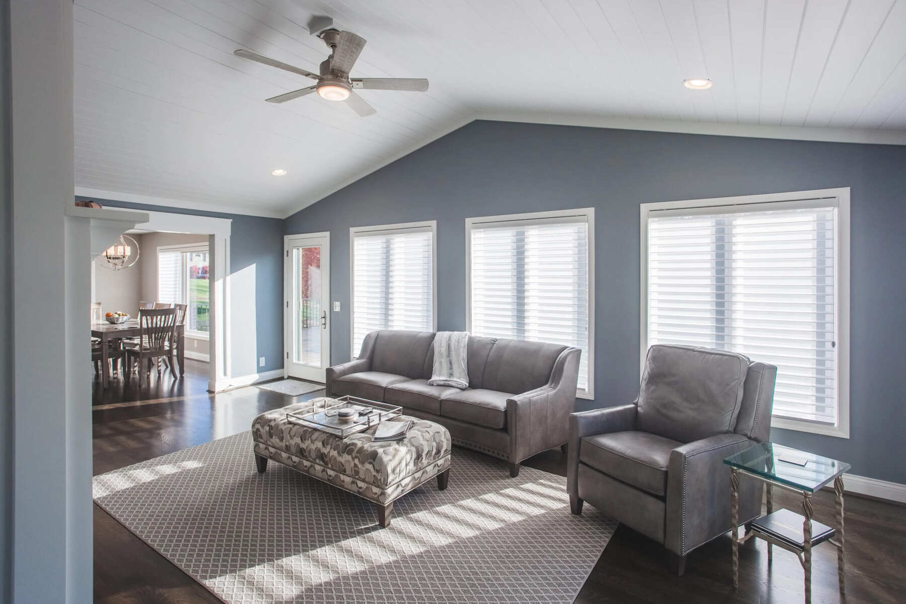 Cincinnati living room with gray sofa, armchair, ottoman, large windows, and ceiling fan in a bright open space