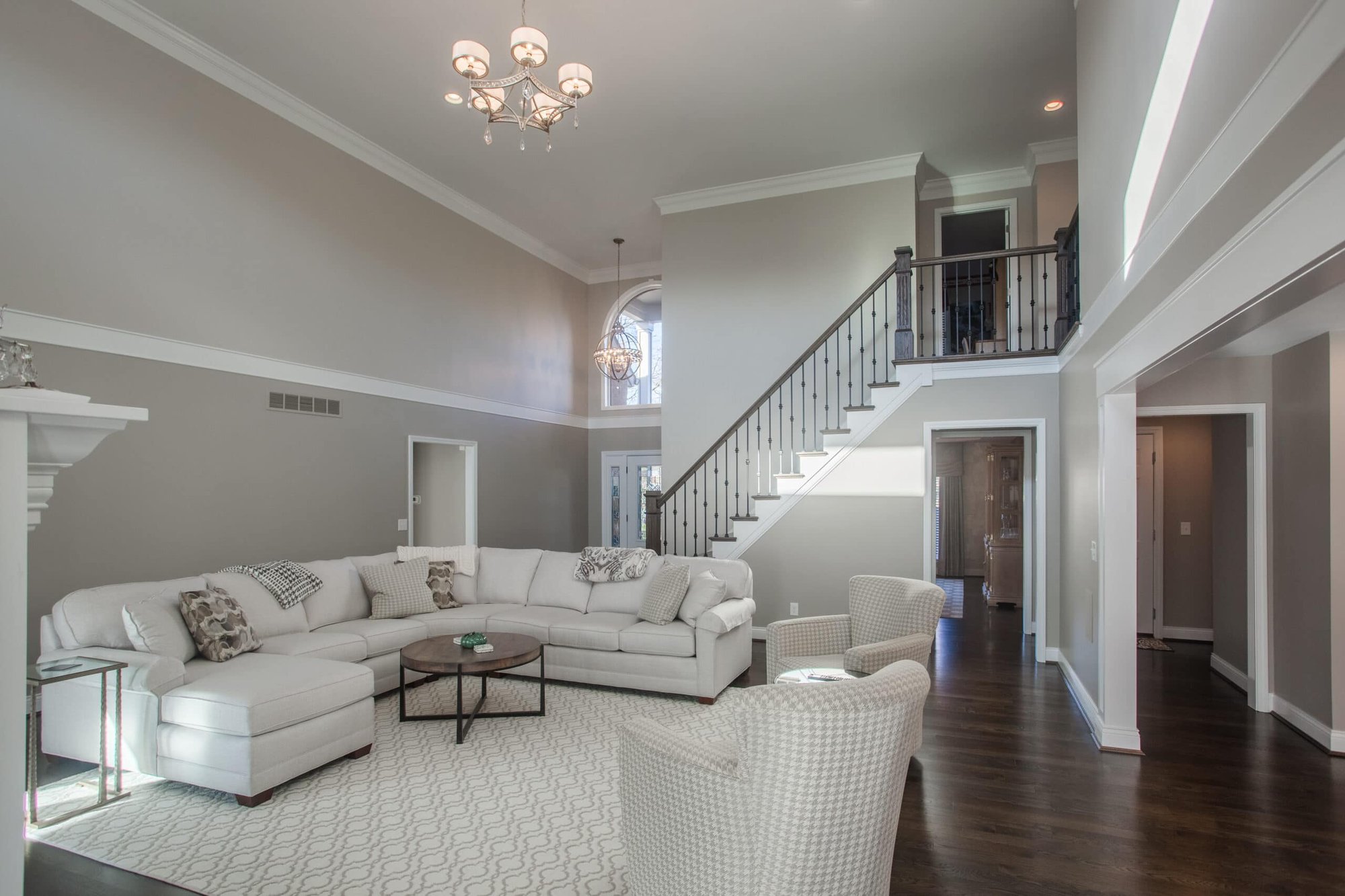 Cincinnati living room with high ceilings, staircase, white sectional sofa, chandelier, and hardwood floors in a bright, open space