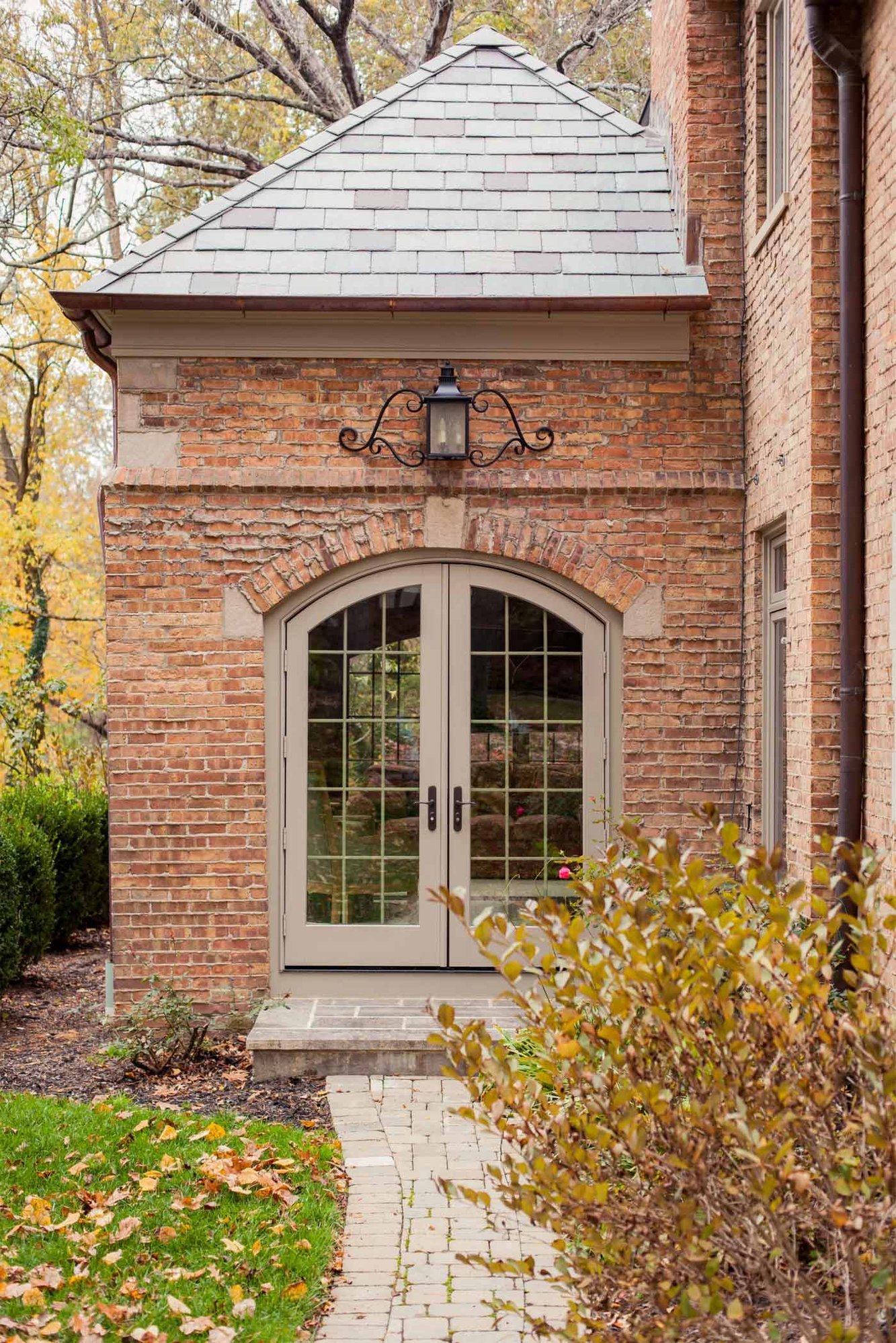 Exterior view of a traditional brick home with arched French doors and a slate roof in the Cincinnati area, surrounded by fall foliage and a landscaped walkway Exterior view of a traditional brick home with arched French doors and a slate roof in the Cincinnati area, surrounded by fall foliage and a landscaped walkway