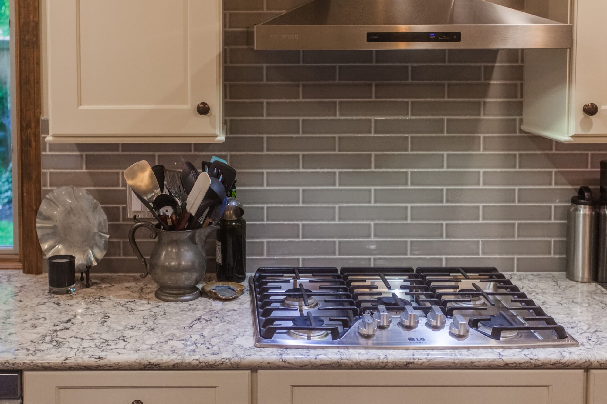 Gas cooktop with stainless vent hood, granite counters, and gray tile backsplash in a Cincinnati kitchen