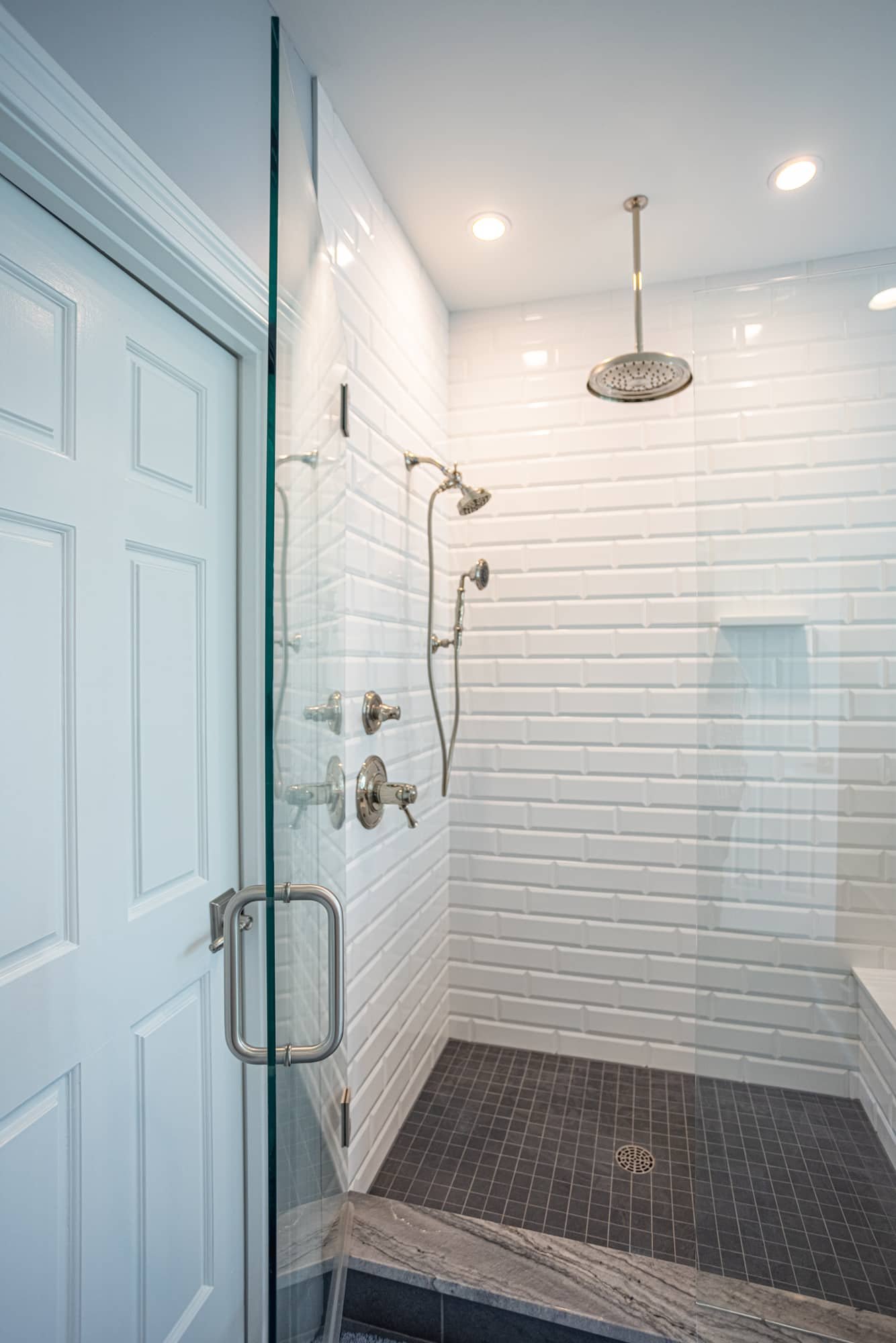 Glass walk-in shower with white subway tile and dark floor by Legacy Builders Group in Greater Cincinnati