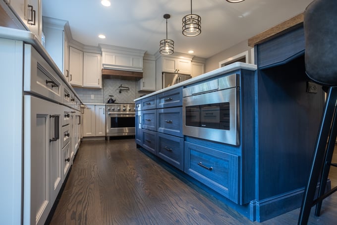 Modern Cincinnati kitchen with white cabinets, dark blue island, stainless steel appliances, and pendant lighting over a spacious layout