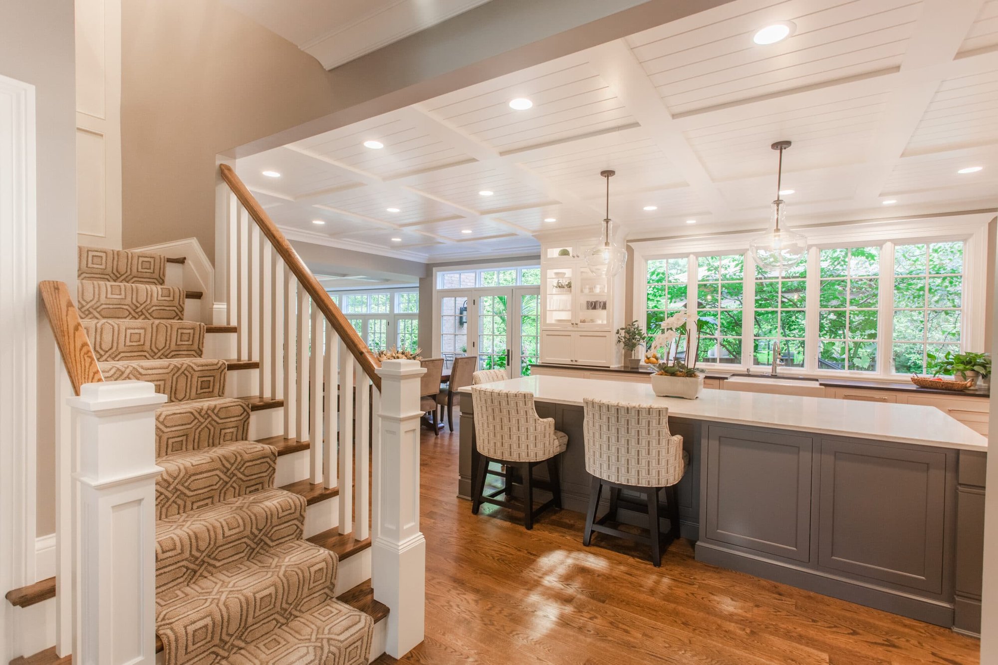 Montgomery, OH kitchen with staircase, gray island, woven stools, coffered ceiling, and large windows