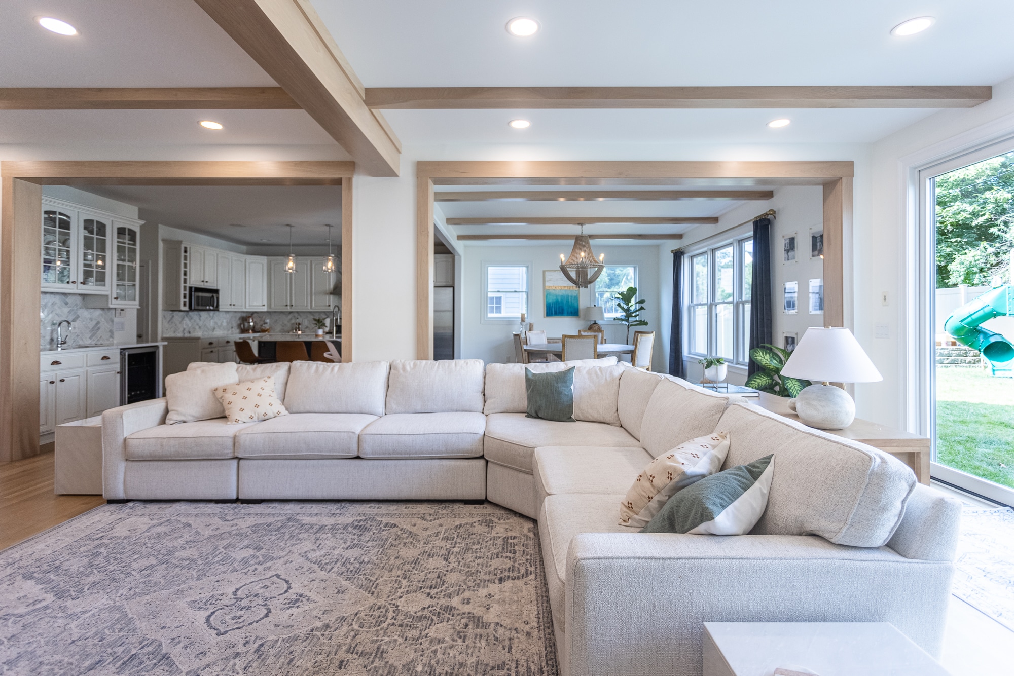 Open living room with sectional sofa, exposed beams, and view to kitchen by Legacy Builders Group in Greater Cincinnati