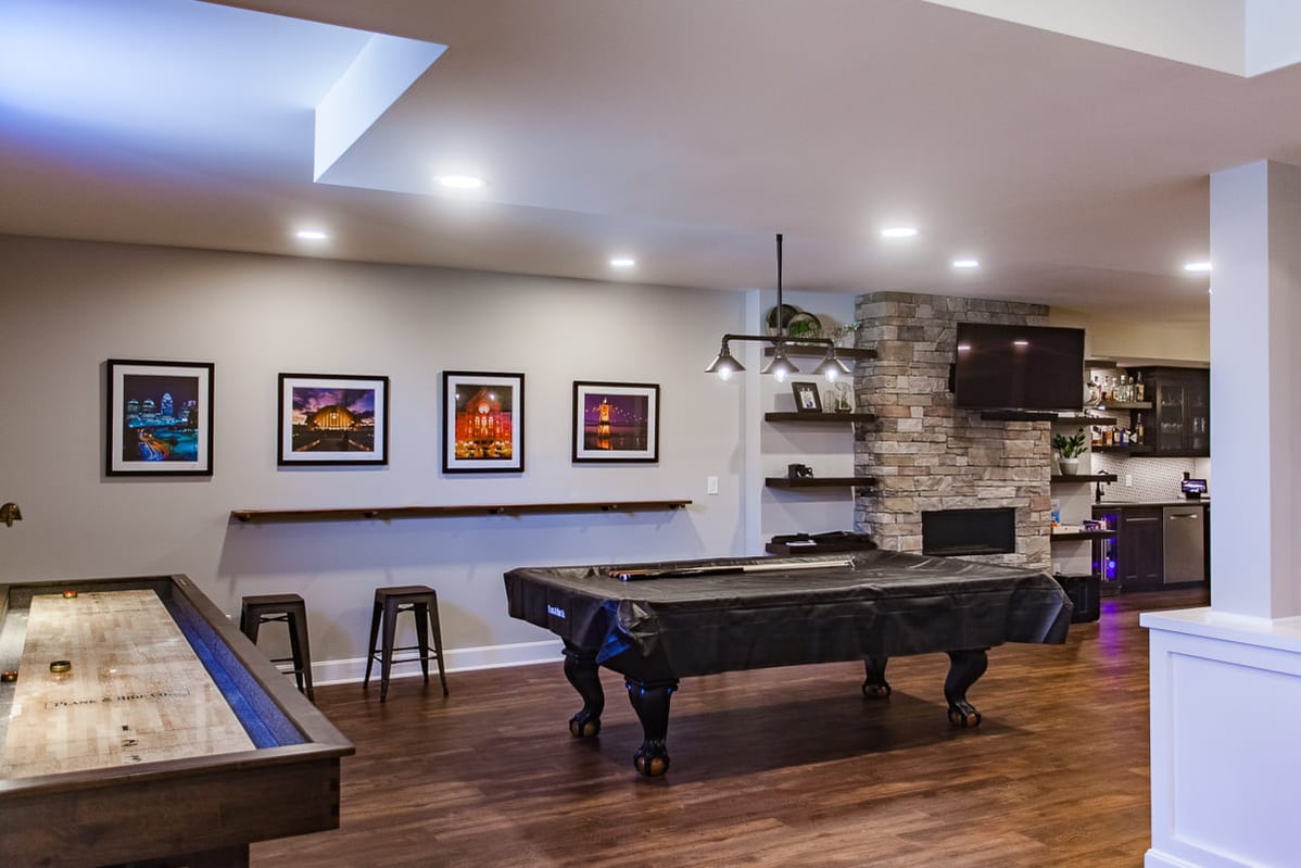 Pool table beneath pendant light in Cincinnati finished basement remodel with fireplace and recessed lighting