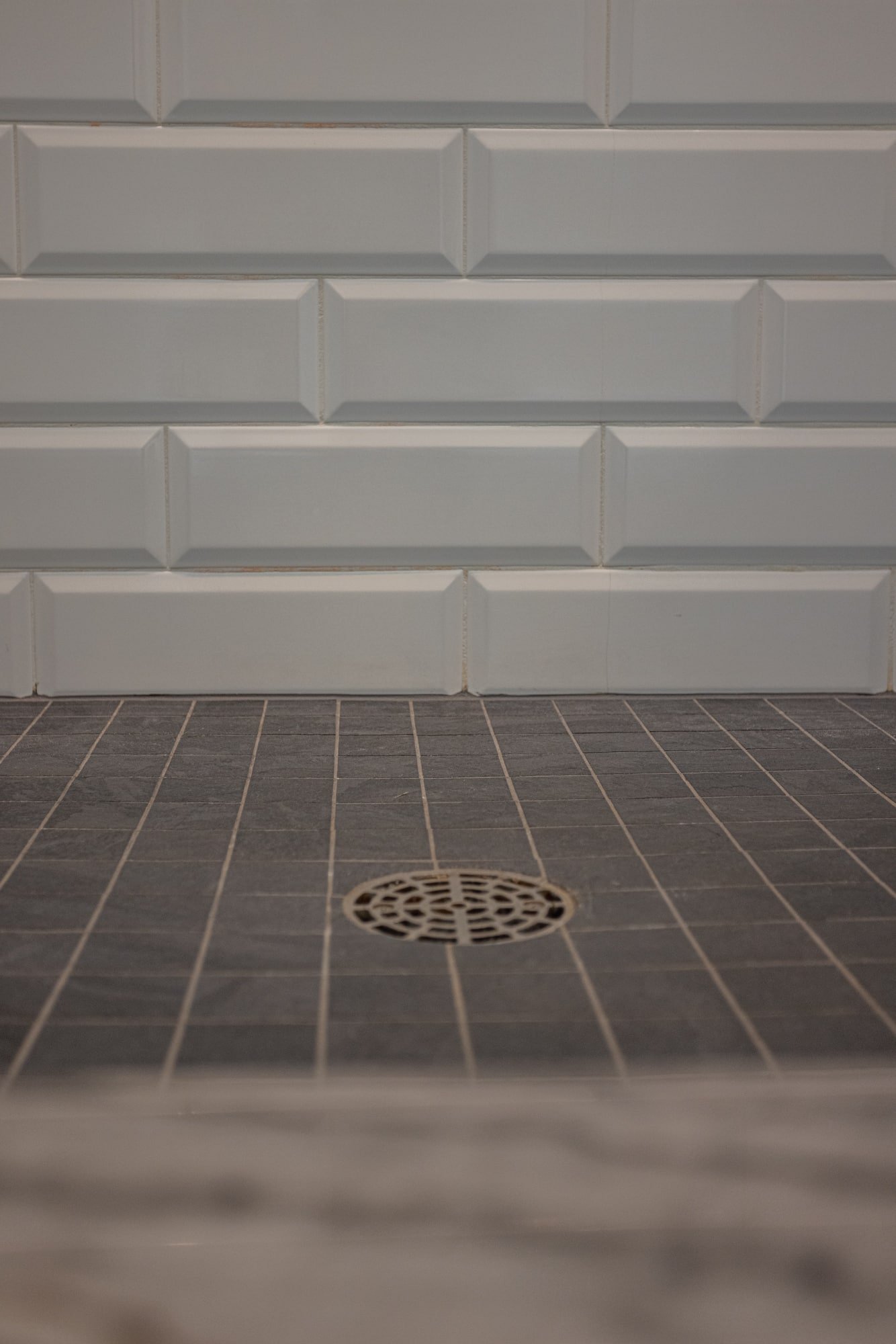 Shower floor with dark tile and drain, white subway tile walls by Legacy Builders Group in Greater Cincinnati