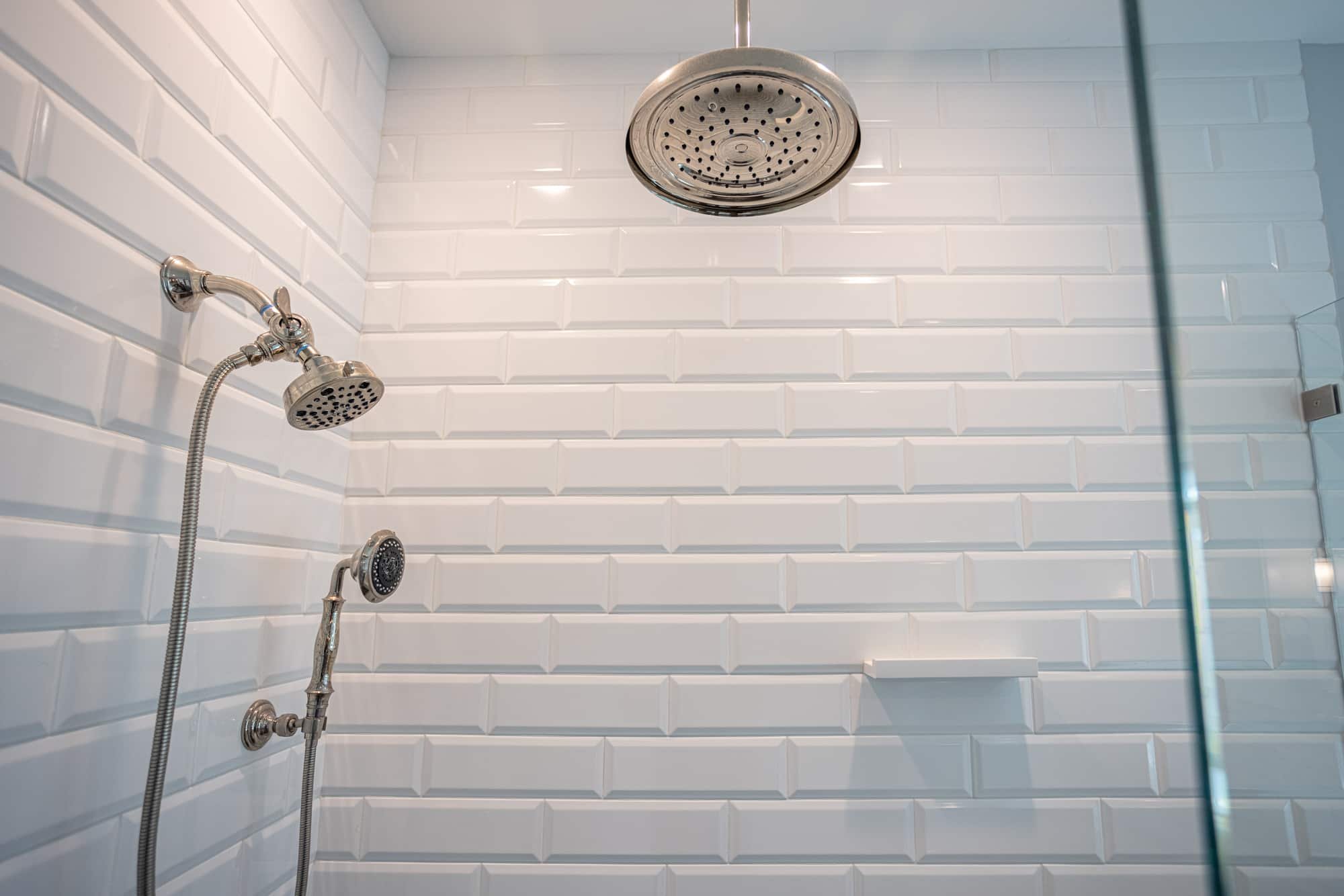 Shower with white subway tile, rain showerhead, and handheld fixture by Legacy Builders Group in Greater Cincinnati