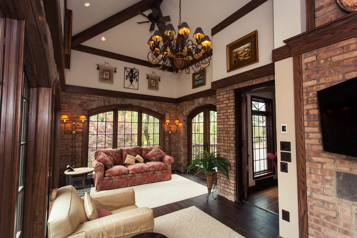 Sunroom addition interior with brick wall details and chandelier hanging from high ceiling by Legacy Builders