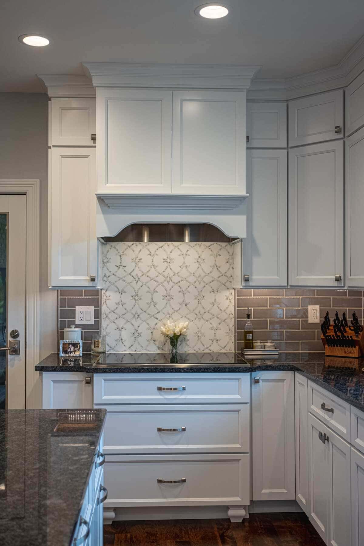 Patterned backsplash behind range hood in kitchen with recessed lighting