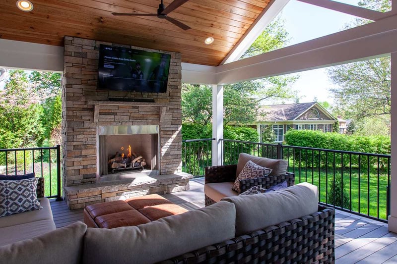 Covered porch interior with vaulted ceiling and stone fireplace beneath mounted TV