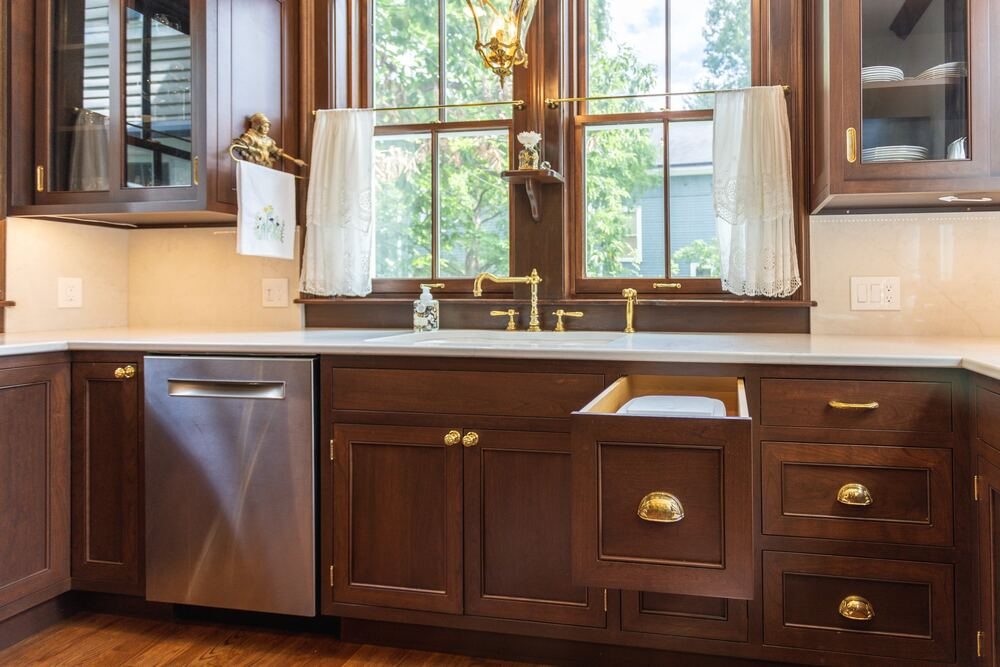 Victorian style kitchen wood cabinets beneath windows with gold hardware