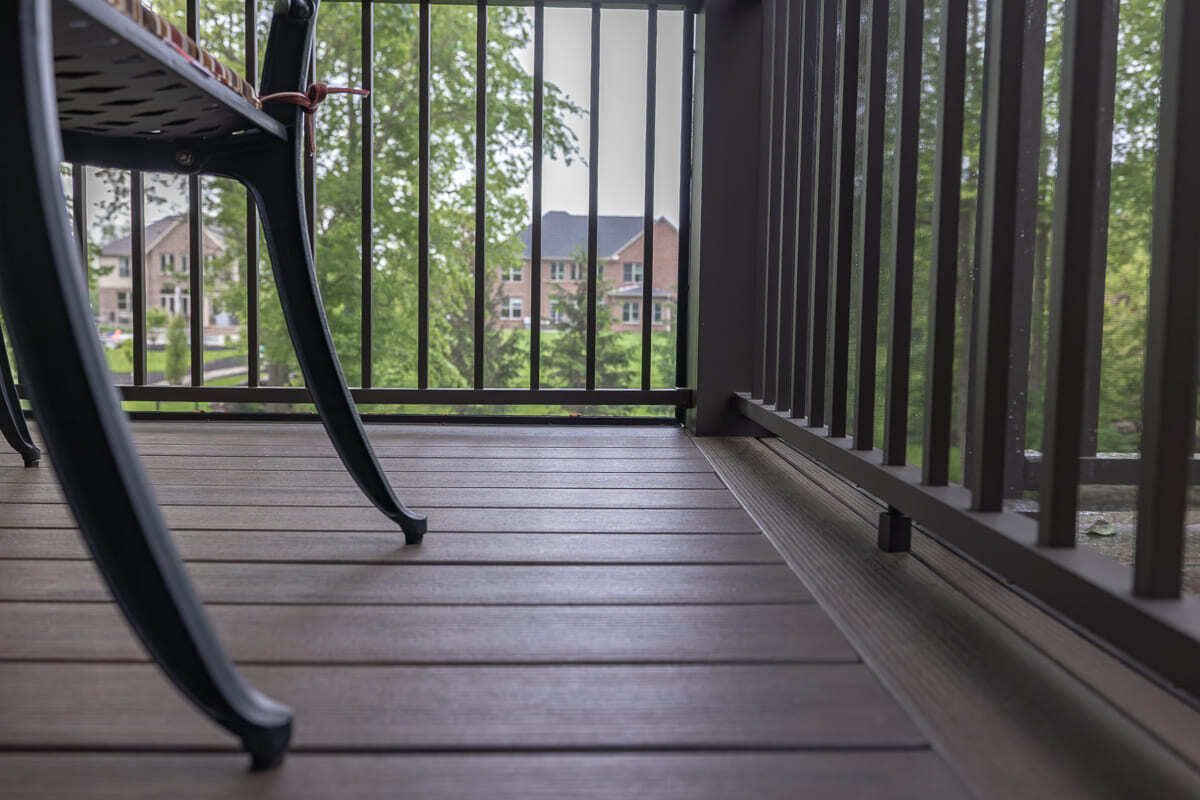 Close-up of wood deck flooring, black railing, screened walls, and outdoor dining chair.