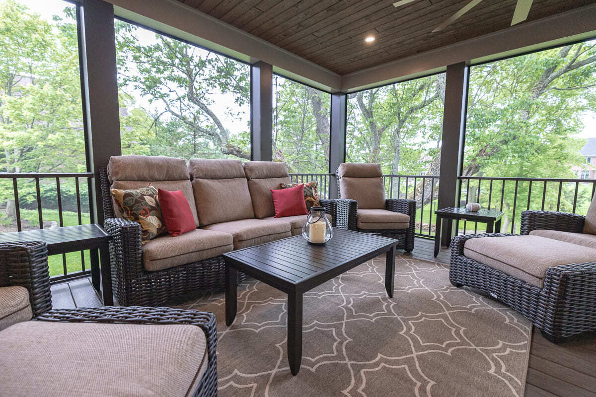 Covered outdoor deck seating area with wicker furniture, wood ceiling, railing, and tree views. Covered outdoor deck seating area with wicker furniture, wood ceiling, railing, and tree views.