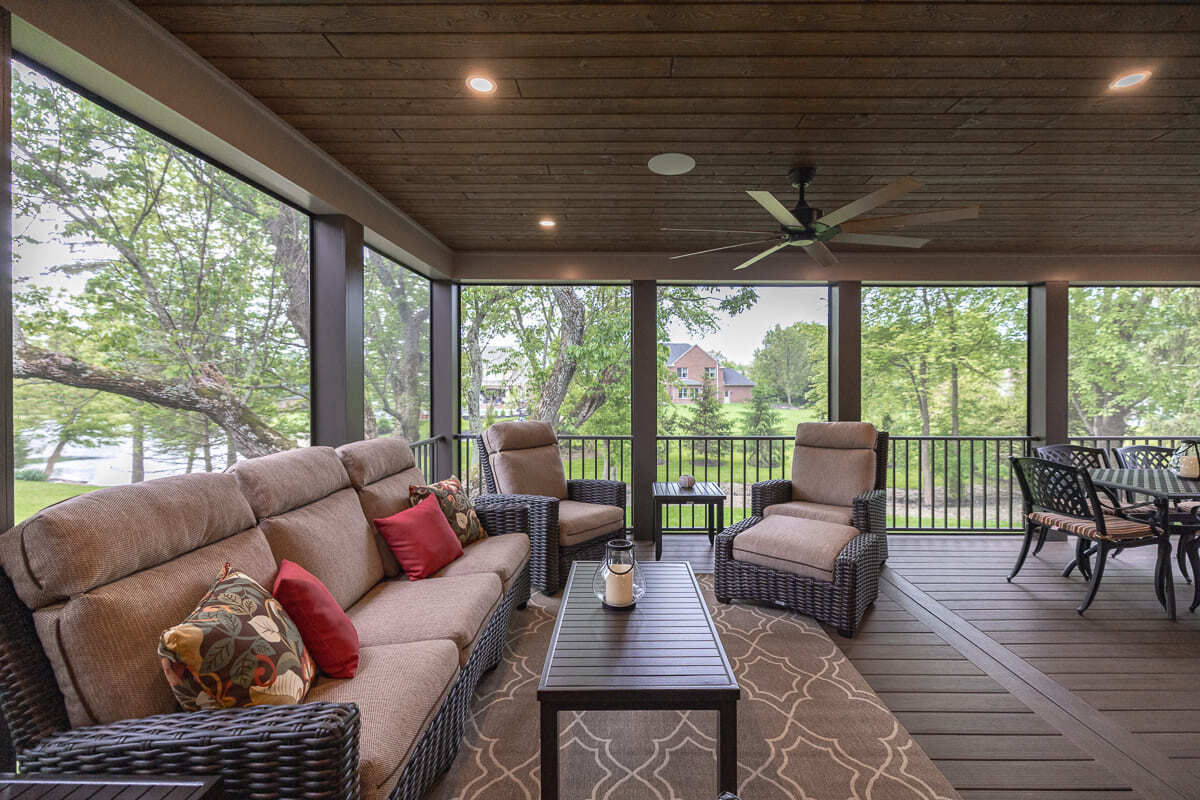Covered outdoor living space with wicker lounge seating, wood deck floor, and screened backyard views.