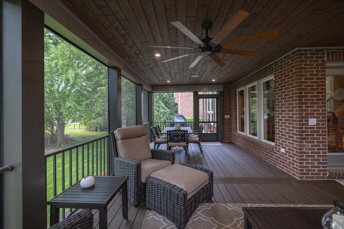 Covered screened deck with wood ceiling, outdoor dining set, lounge chair, and backyard views.
