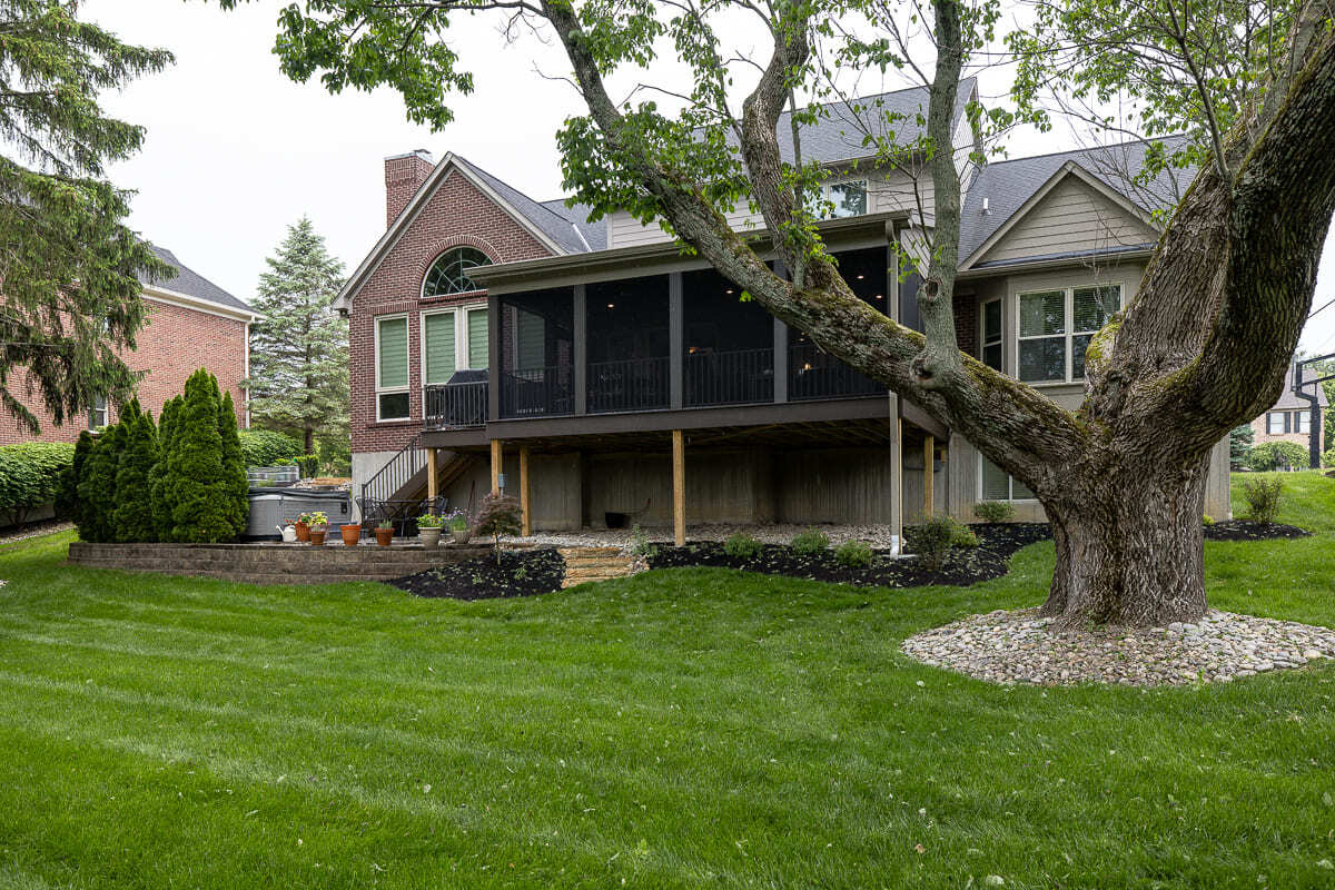 Large screened outdoor deck overlooking a green backyard with mature trees and patio space.