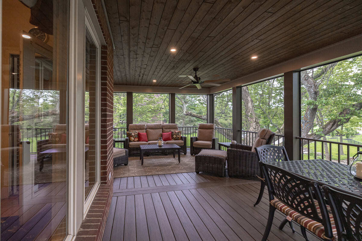 Long screened deck with wood flooring, wicker lounge seating, dining area, and backyard views.