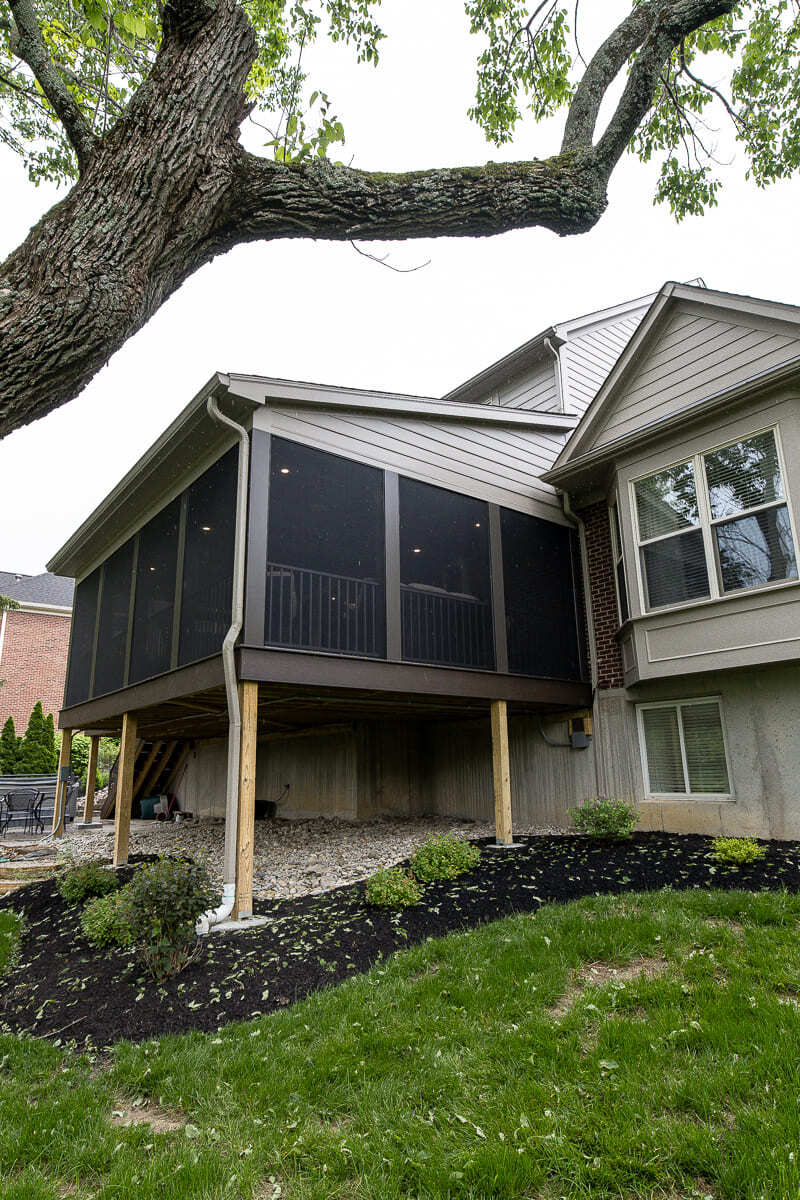 Screened deck with wood support posts, dark railing, and landscaped backyard.