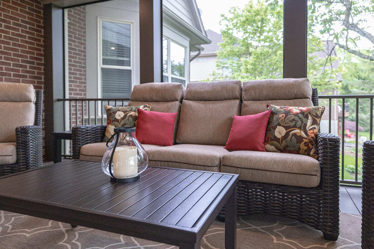 Screened outdoor deck lounge with wicker sofa, wood table, patterned rug, and backyard views.