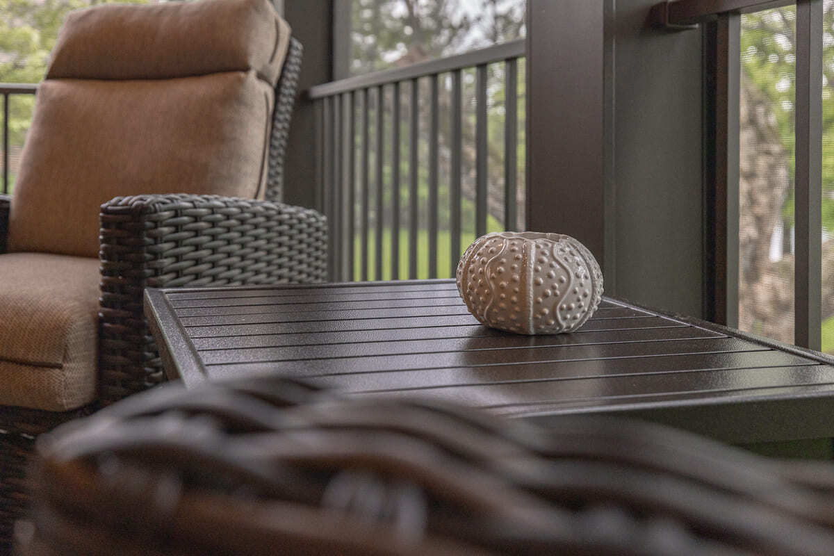 Screened outdoor deck seating area with wood table, railing, wicker chair, and backyard views.