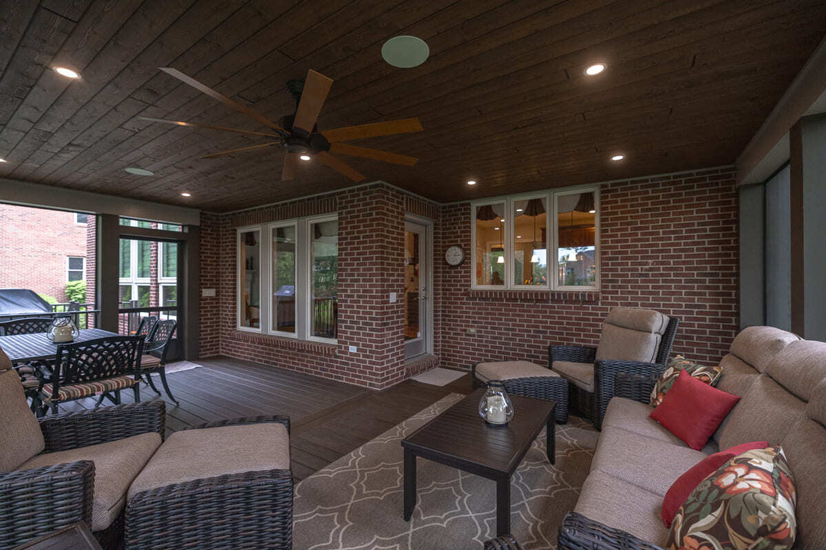 Screened outdoor deck with wood ceiling, ceiling fan, dining area, and wicker lounge seating.