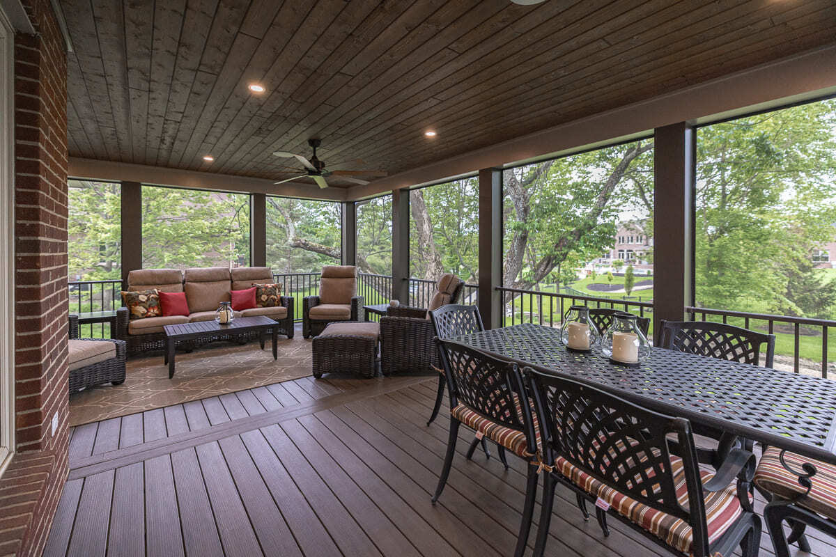 Spacious screened deck with wood flooring, dining table, wicker lounge seating, and tree views.