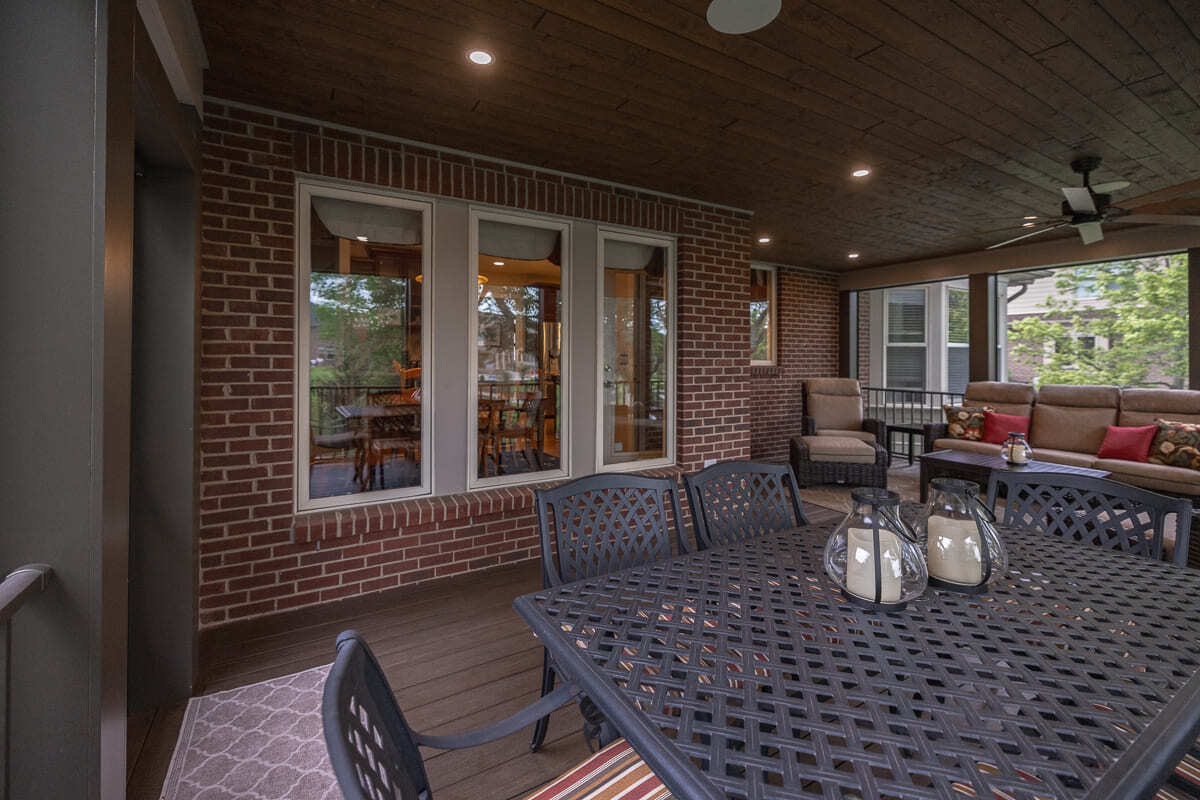 Spacious screened outdoor deck with dining table, wood floor, brick wall, and lounge area.