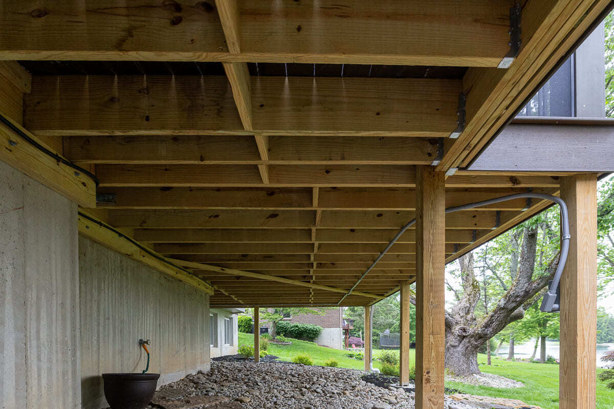 Under-deck view showing wood framing, support posts, gravel bed, and backyard landscaping.