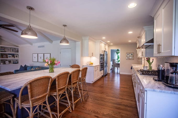 Kitchen in Greater Cincinnati with white cabinets, marble island, rattan barstools, and open layout to living room