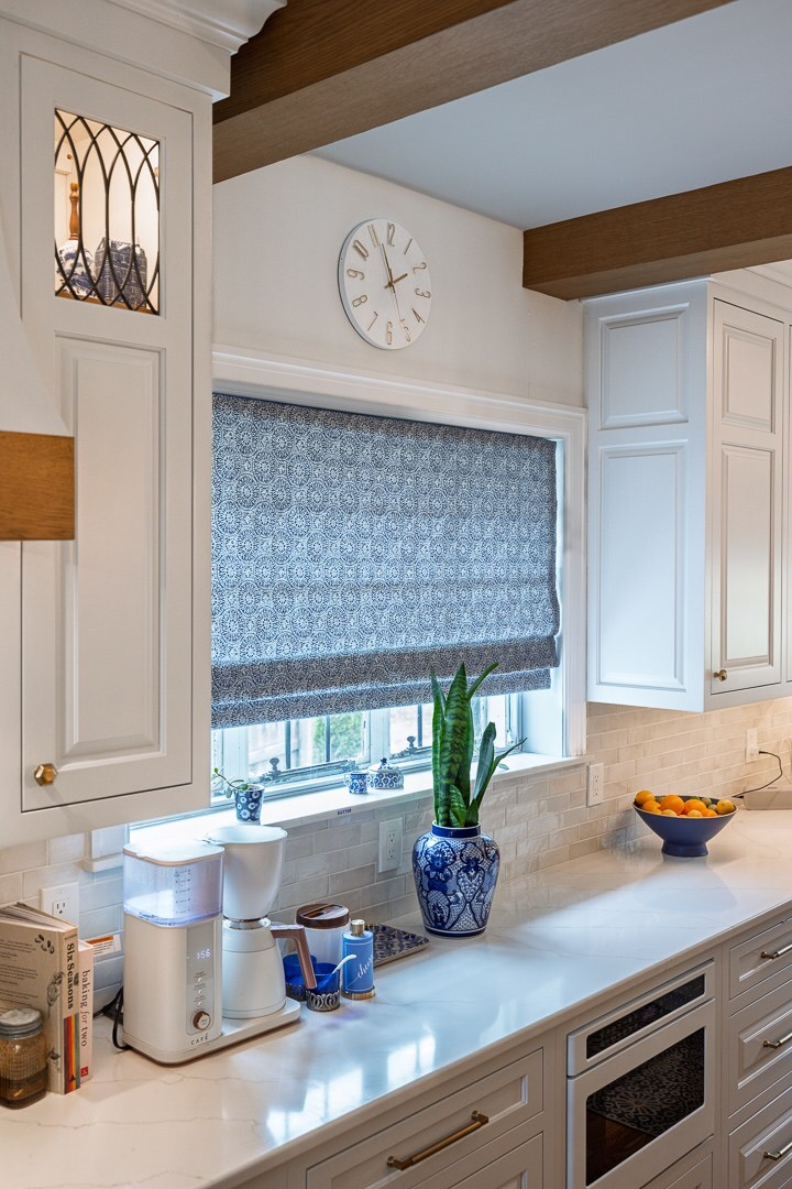 Cincinnati kitchen counter with white cabinetry, window shade, potted plant, coffee maker, and brass hardware accents