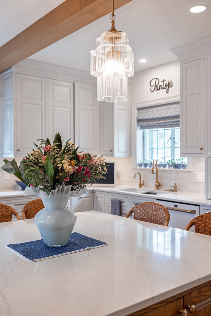 Cincinnati kitchen island with white countertop, floral arrangement, pendant lighting, and white cabinetry with brass fixtures in a bright space