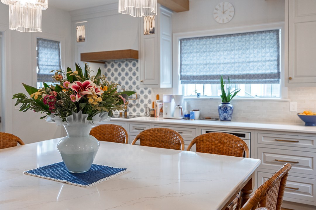 Cincinnati kitchen island with white countertop, woven bar stools, floral centerpiece, and bright cabinetry with window light