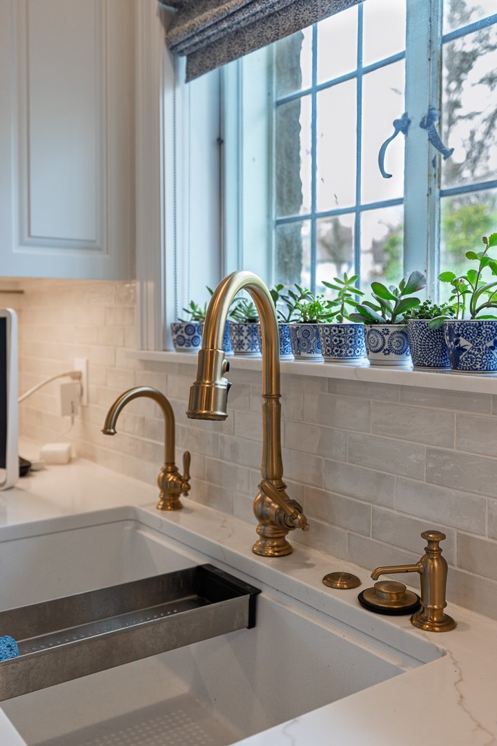 Cincinnati kitchen sink with brass faucet, white farmhouse basin, tile backsplash, and potted plants along a bright window sill
