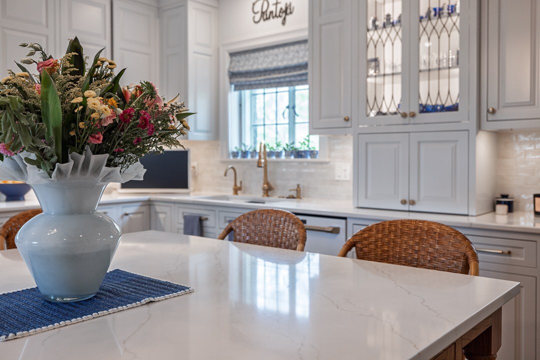 Cincinnati kitchen with white cabinetry, brass fixtures, woven stools, large island, and floral centerpiece in a bright, inviting space